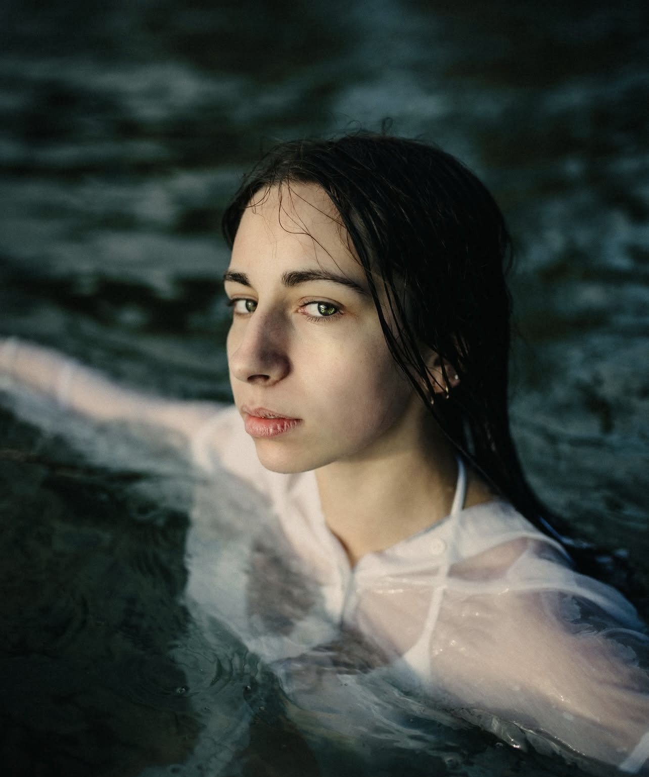 Levi Price standing waist deep in a lake, holding a camera, surrounded by sunlight reflecting on the water. A candid portrait capturing his passion for filmmaking and love of water.